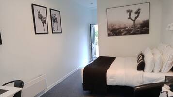 A hotel room with a bed, a desk, and chairs. There are two framed pictures on the wall and a large painting above the bed.