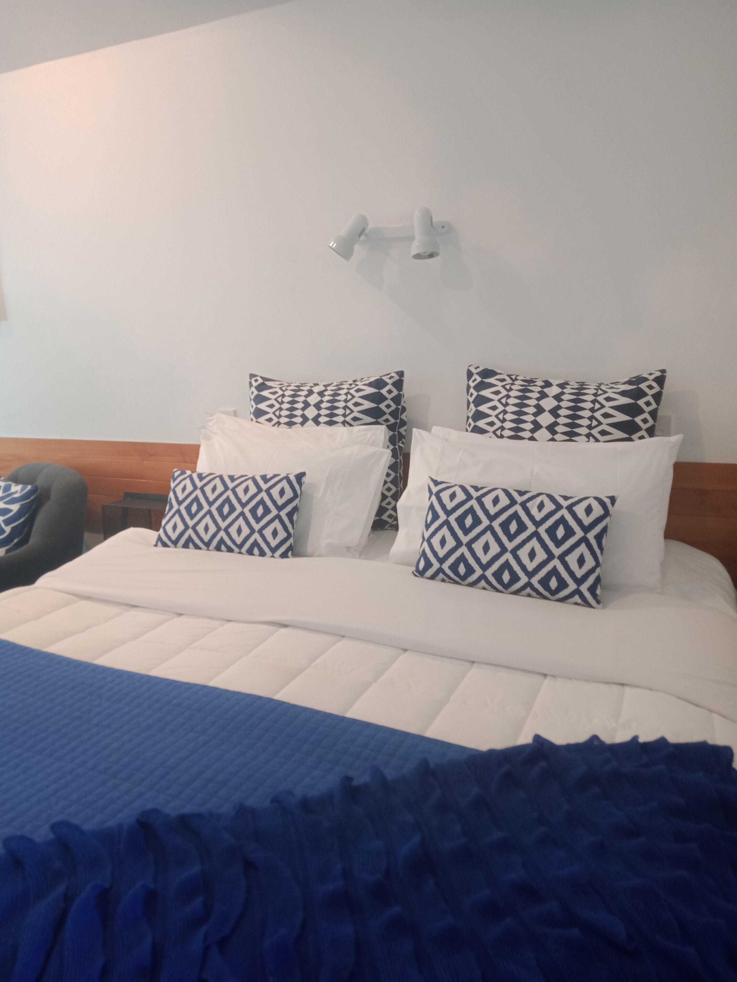 A neatly made bed with patterned pillows, a blue throw blanket, and a wooden headboard.