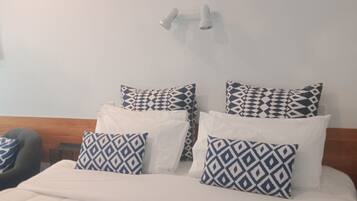 A neatly made bed with patterned pillows, a blue throw blanket, and a wooden headboard.