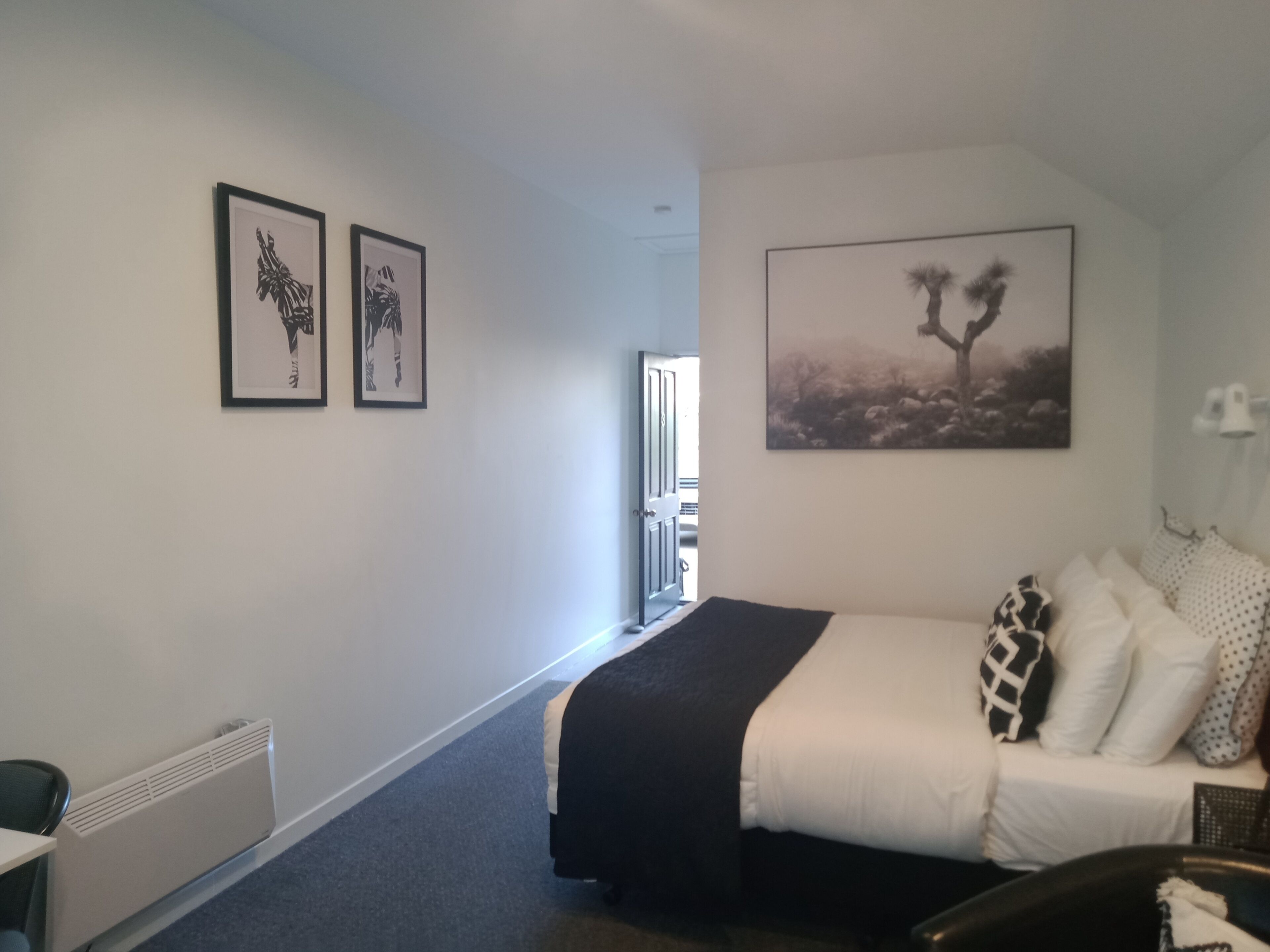 Quarto de hotel com cama, escrivaninha e duas fotos emolduradas na parede.