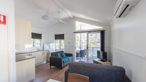 A modern kitchen with wooden cabinets, a dining area with a table and chairs, a grey sofa with a striped cushion, and a TV on a small table. - Main Beach Tourist Park (Main Beach)