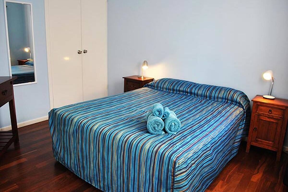 A bedroom with a bed, wooden nightstands, a wardrobe, and a mirror.