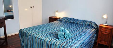 Une chambre à coucher avec un lit, des tables de chevet en bois, une armoire et un miroir.