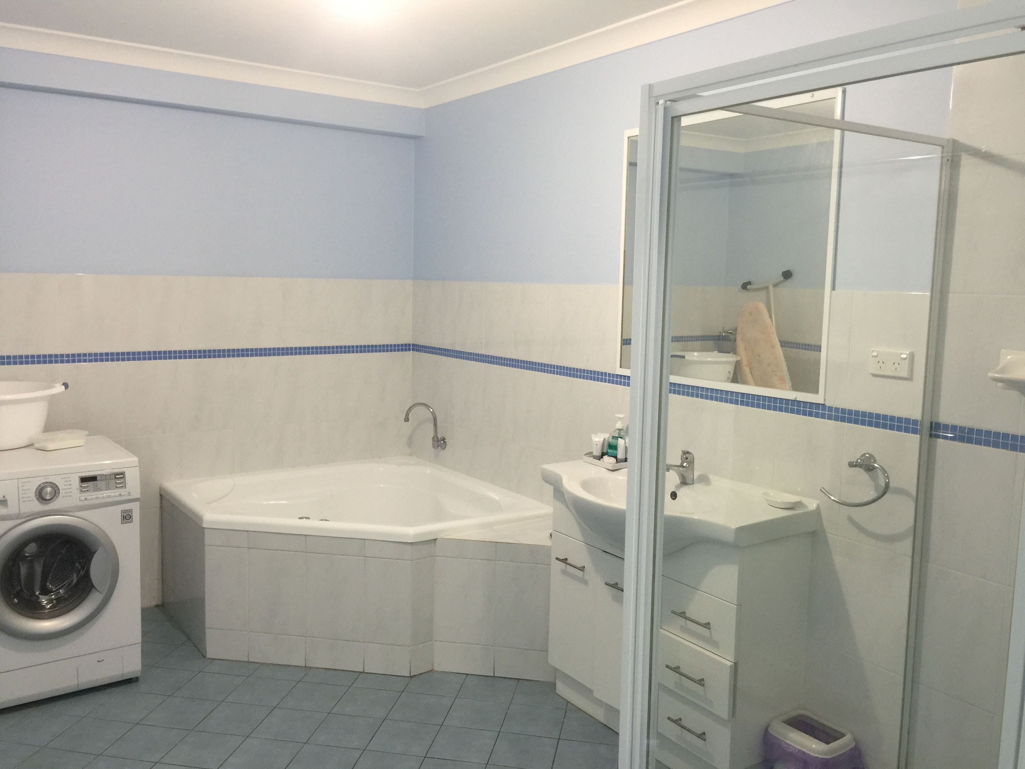 A bathroom with a washing machine, a bathtub, a sink, and a glass shower enclosure.