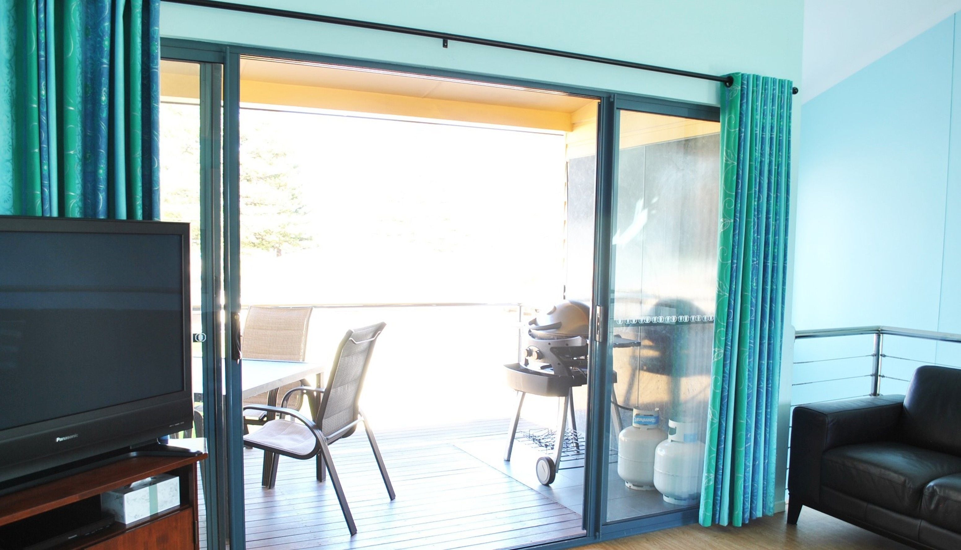 A living room with a television, a sofa, a sliding glass door leading to an outdoor area with a grill and chairs.