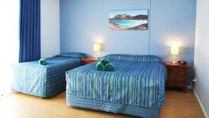 Habitación de hotel con dos camas, una mesita de noche con lámparas, un cuadro de un paisaje y suelo de madera.