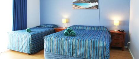 A hotel room with two beds, a nightstand with lamps, a painting of a landscape, and a wooden floor.