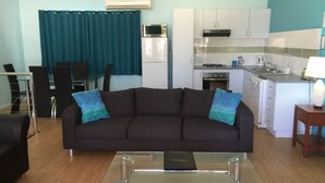 Una sala de estar con un sofá oscuro, una mesa de centro de vidrio y cortinas color turquesa.