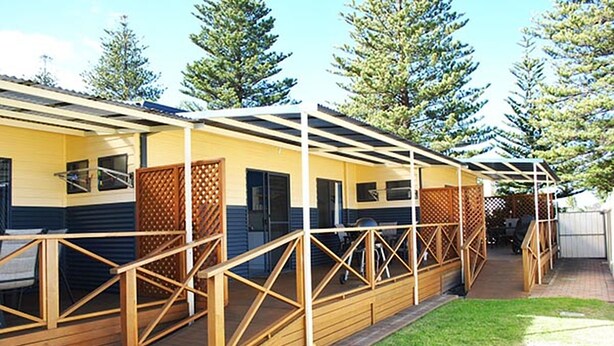 Una hilera de cabañas de madera con un porche cubierto y un área de terraza cercada.