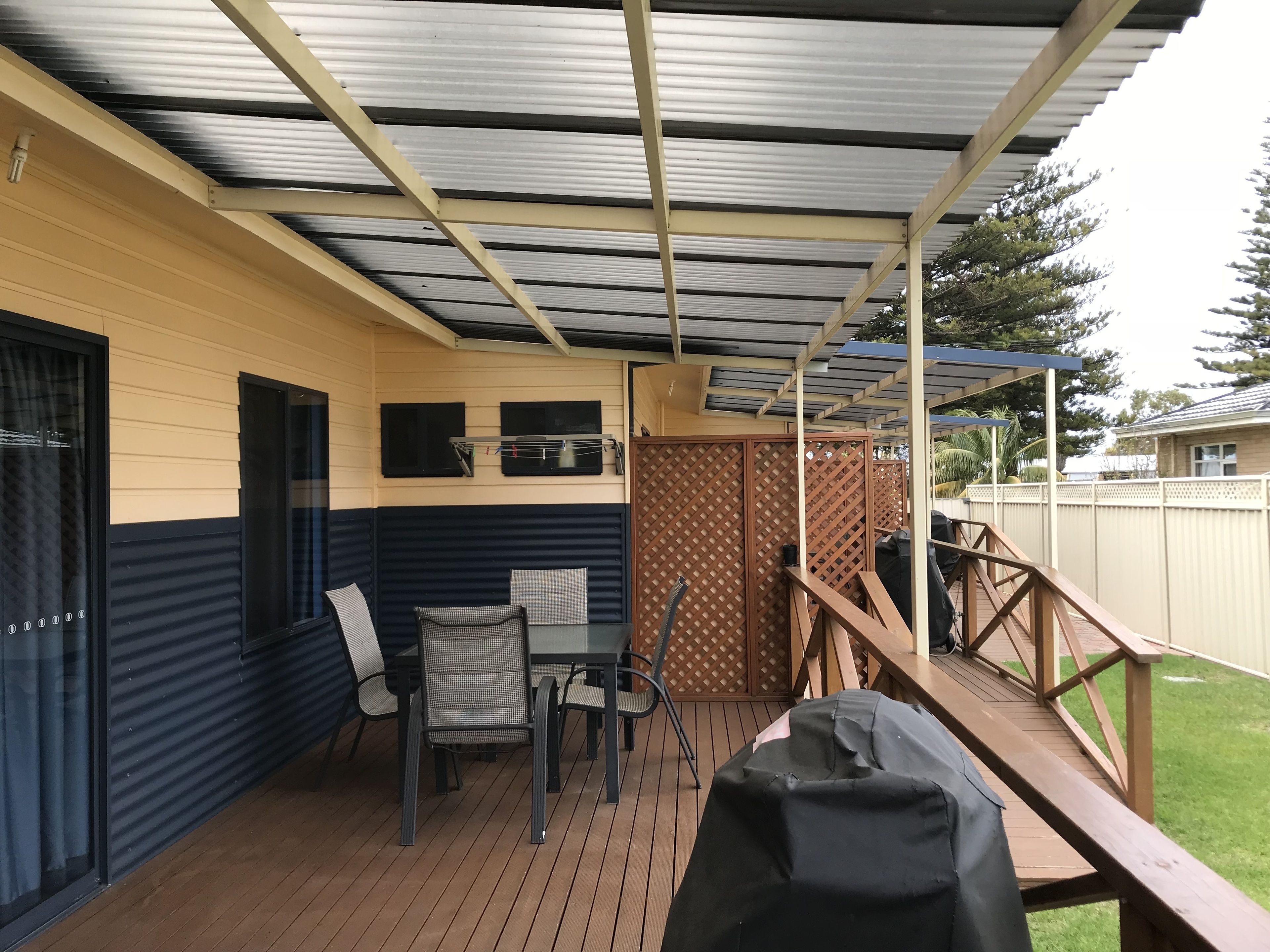 A covered patio with a wooden deck, a table with chairs, and a barbecue grill.