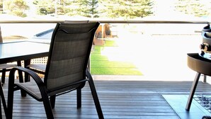 Una terraza con mesa y sillas, una parrilla y vista a un jardín con árboles.