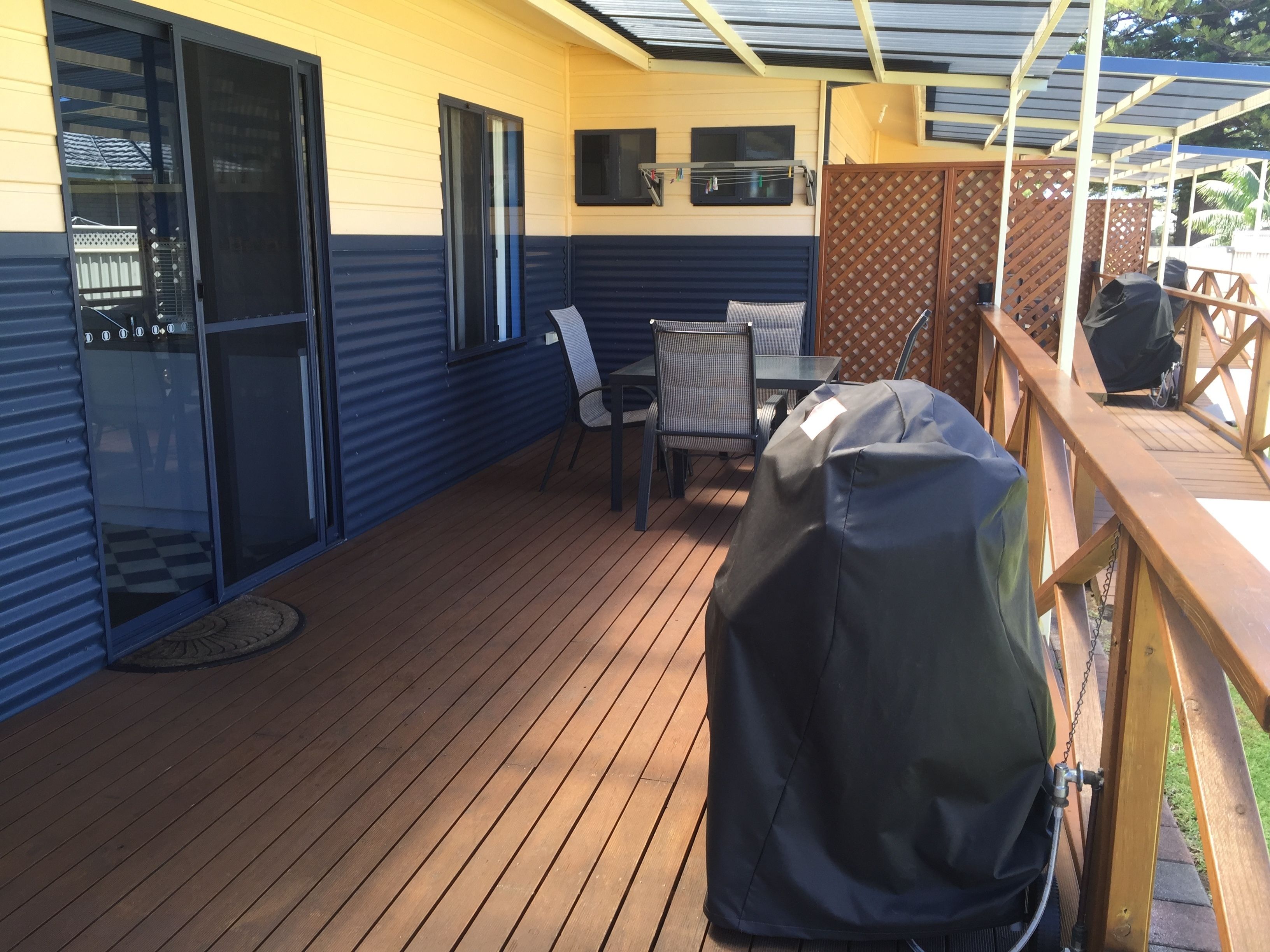 A covered deck with a grill, outdoor seating, and a view of the backyard.