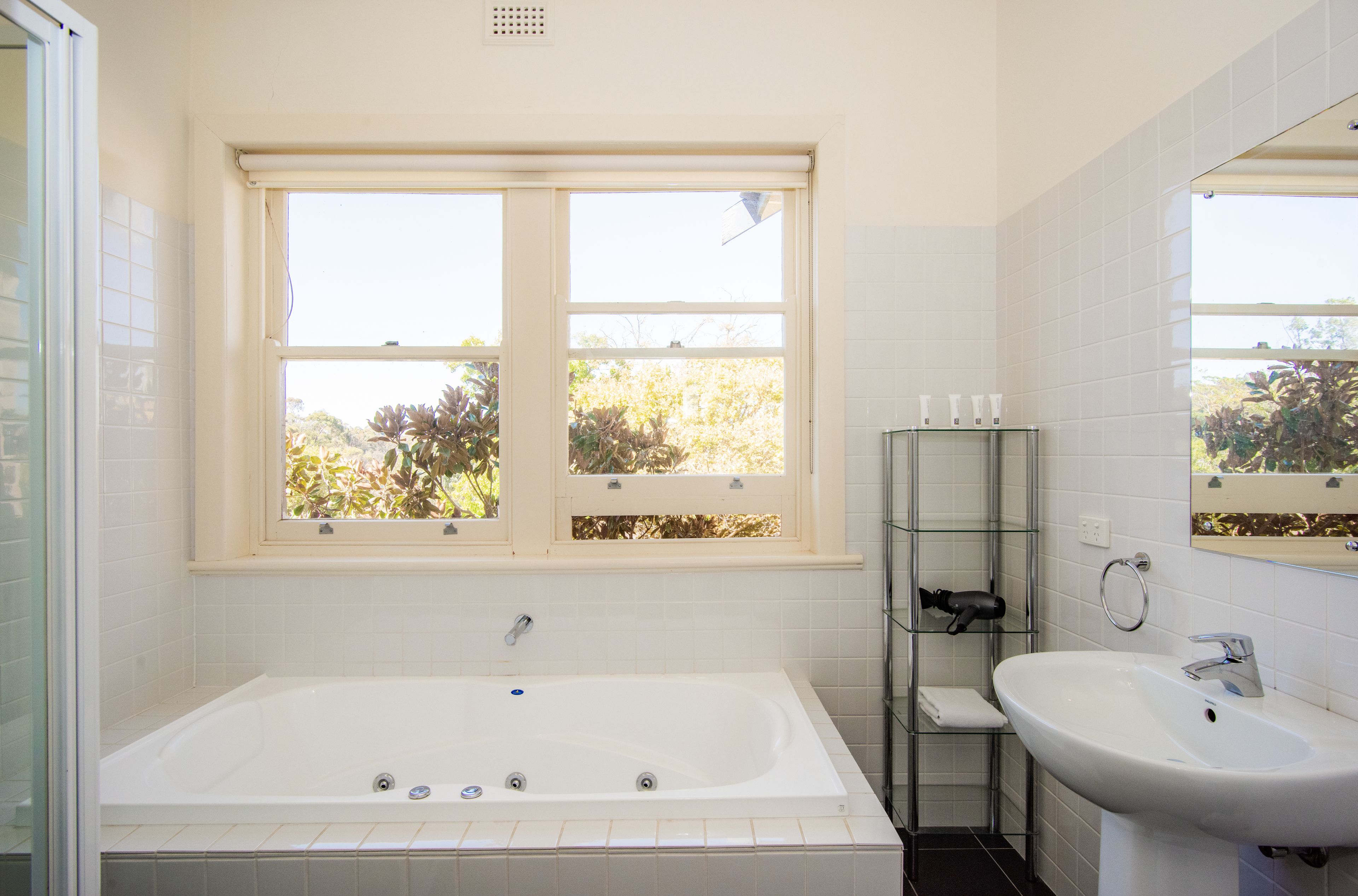 A bathroom with a bathtub, a sink, and a window with a view of trees.