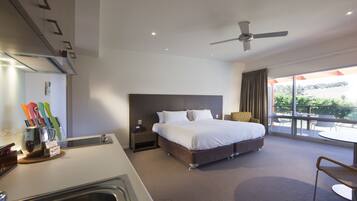 Ein Hotelzimmer mit Bett, Schreibtisch, Stuhl, Deckenventilator und einem Balkon mit Sitzgelegenheit.