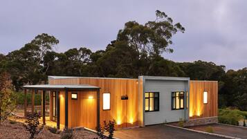 A modern two-story building with a wooden facade and large windows, surrounded by trees.