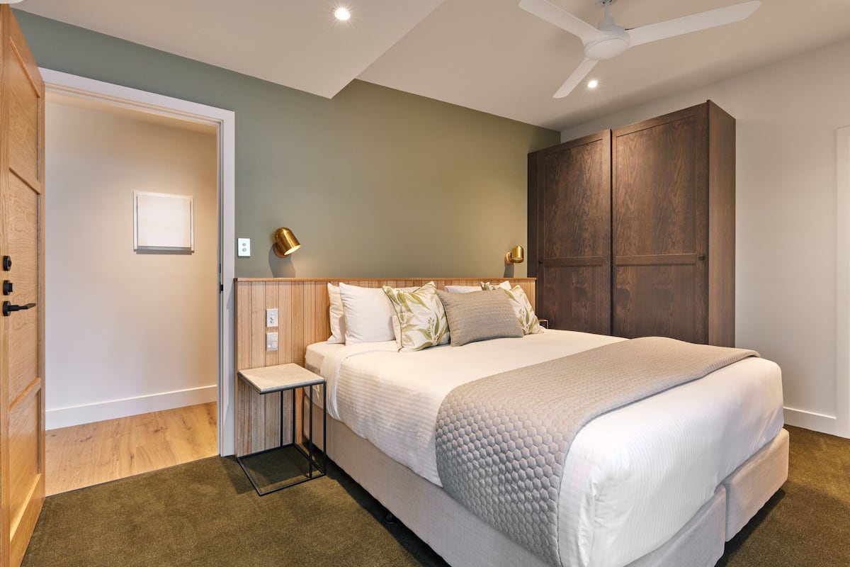 Un dormitorio con una cama grande, lámparas de noche, un armario de madera y una puerta a un pasillo.