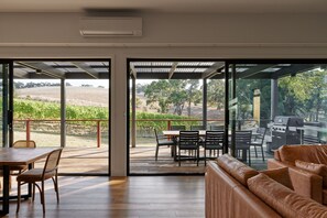 Un interior moderno con una mesa y sillas de madera, un sofá de cuero y un ventanal de vidrio que da a un patio exterior con una parrilla.
