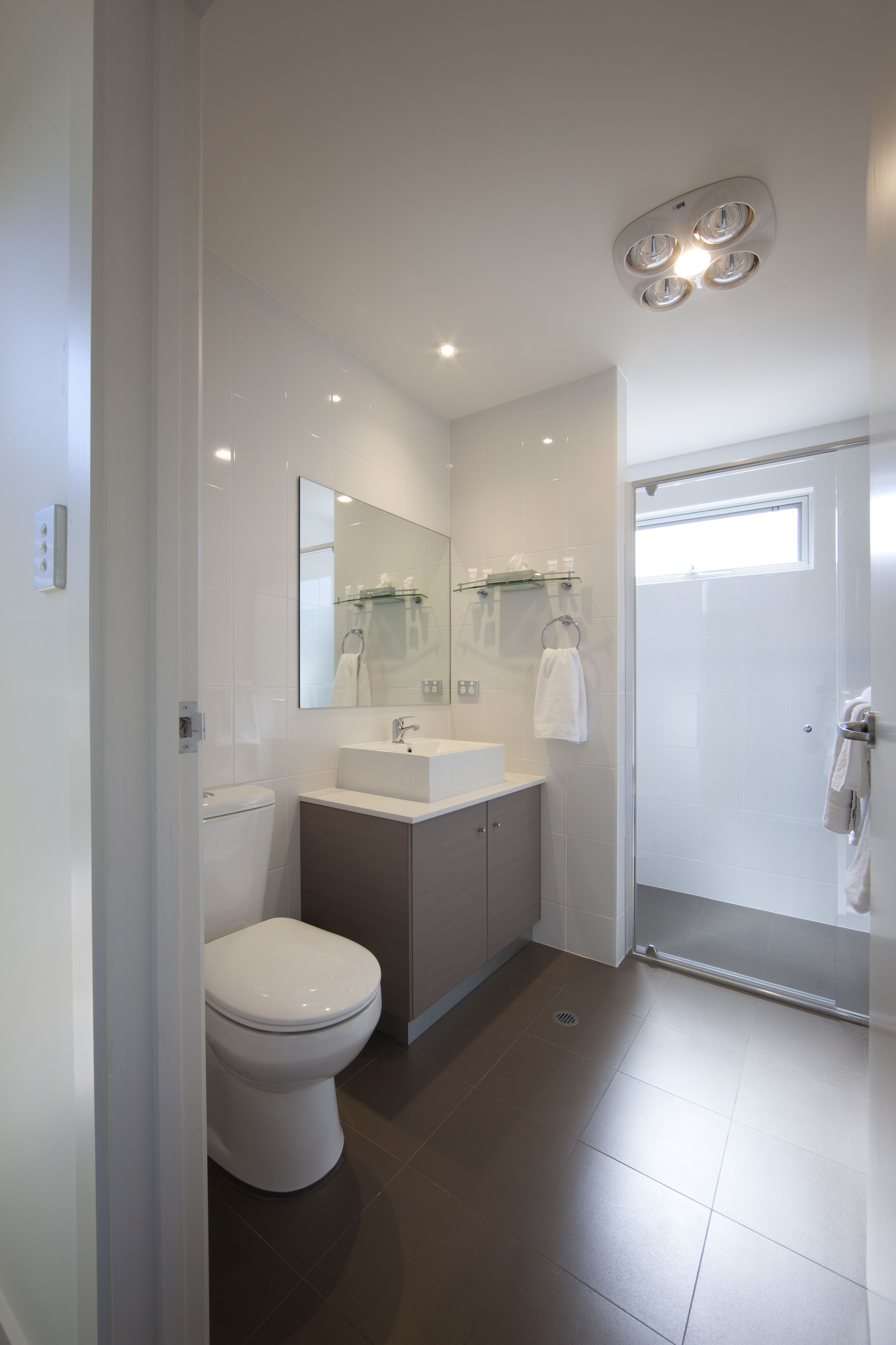 A modern bathroom with a toilet, sink, mirror, and shower.