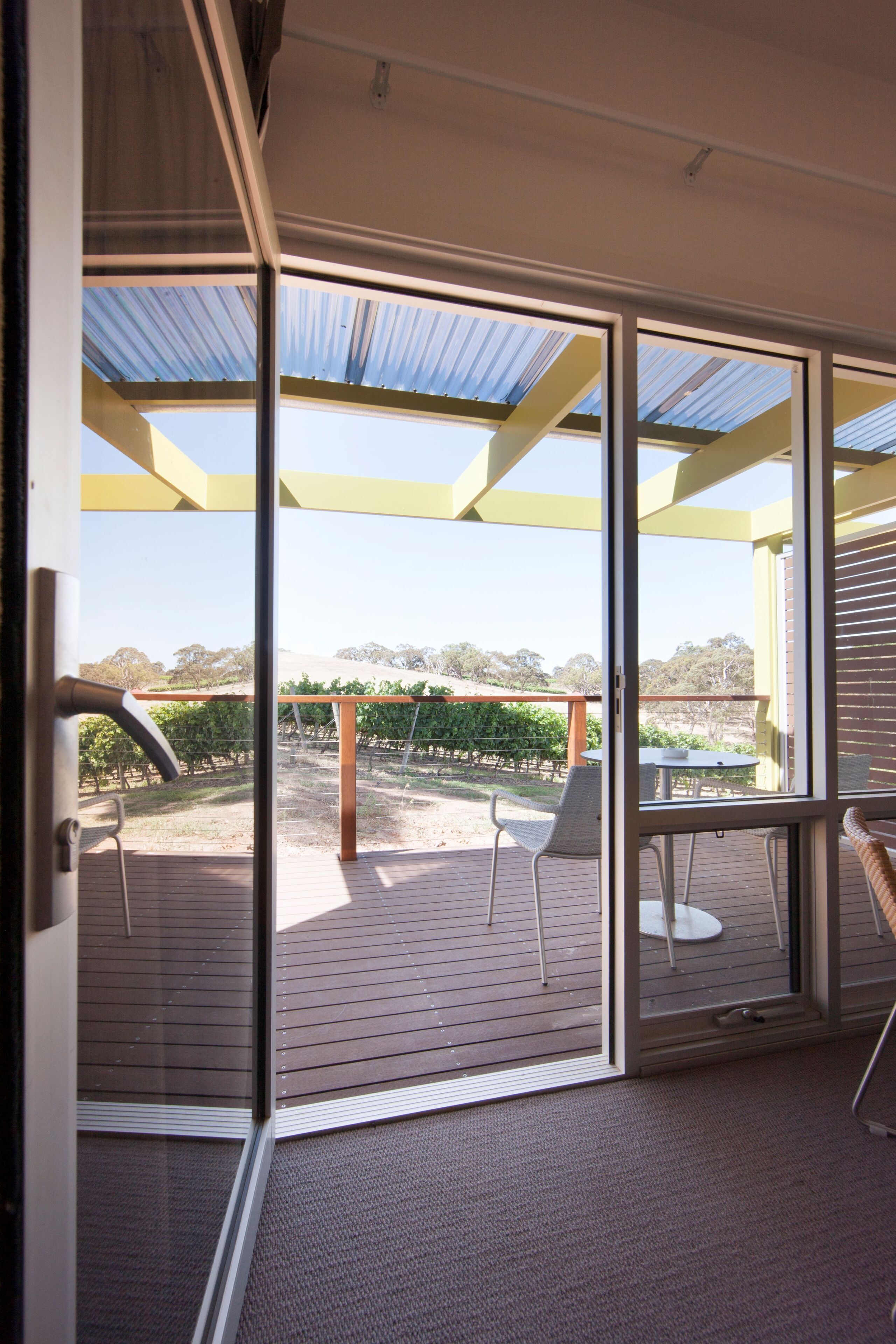 A glass door leading to an outdoor patio with a pergola, chairs, and a view of a vineyard.