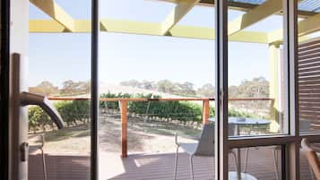 A glass door leading to an outdoor patio with a pergola, chairs, and a view of a vineyard.