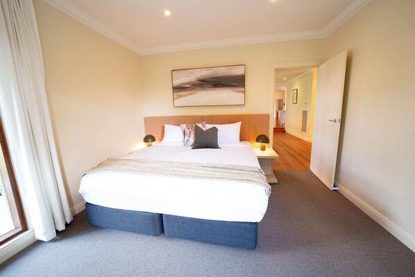A hotel room with a large bed, bedside lamps, a painting on the wall, and a view of the hallway.
