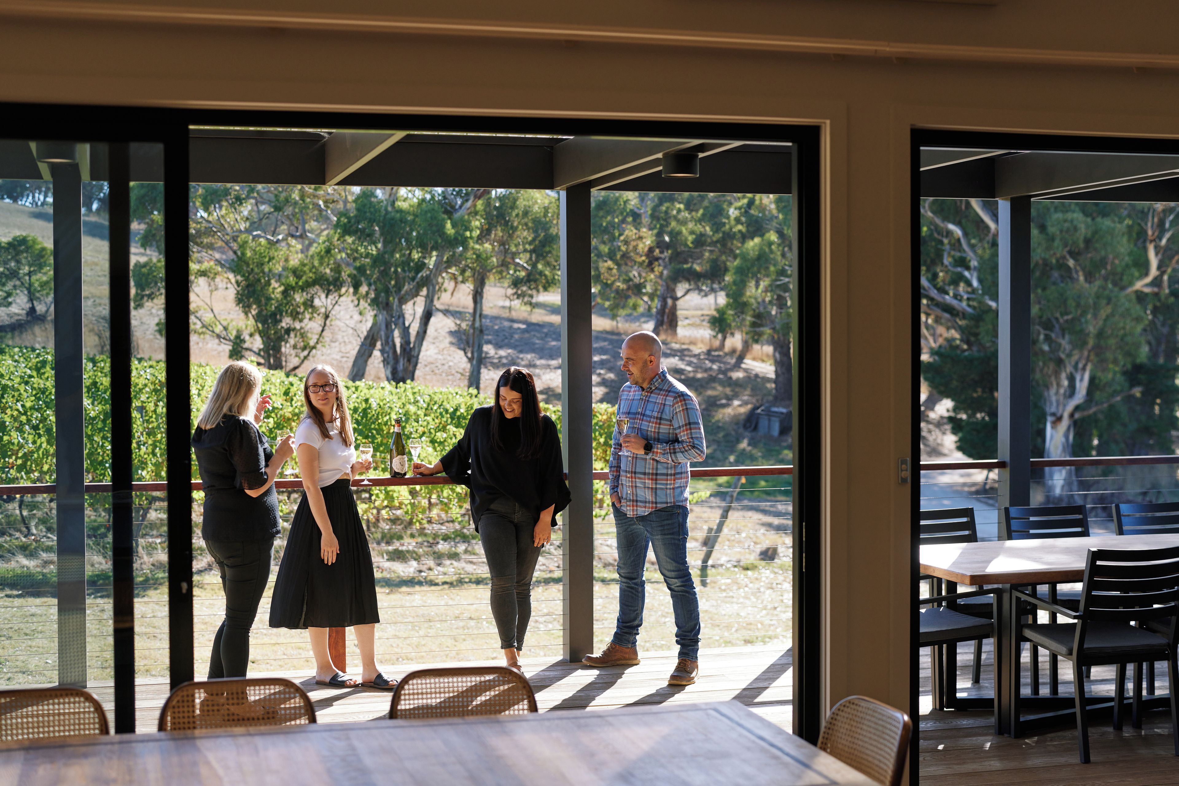 Eine Gruppe von Menschen steht in einem halboffenen Raum mit Blick auf einen Weinberg durch große Fenster.