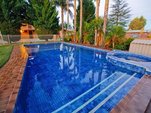 A rectangular swimming pool with blue tiles, surrounded by a brick patio and palm trees. - River City Motel (Mildura)