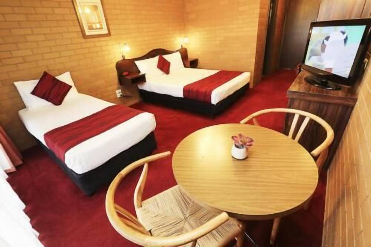 A hotel room with two beds, a television, a round wooden table, and a chair.