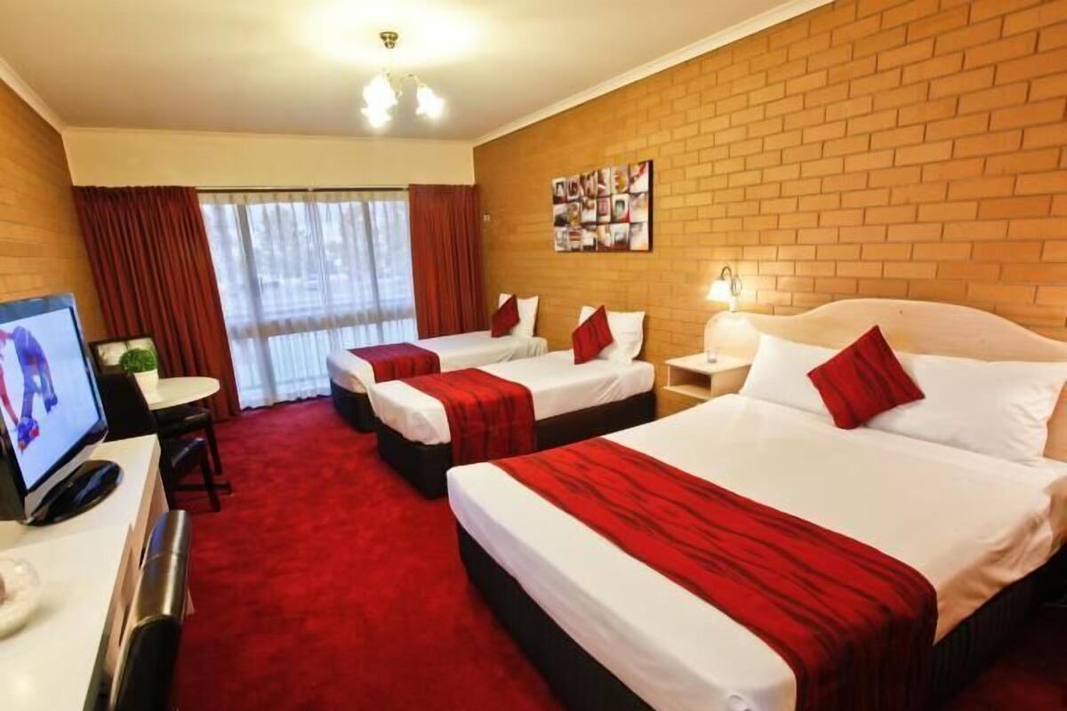 A hotel room with two beds, a desk with a computer, a TV, and a red carpet.
