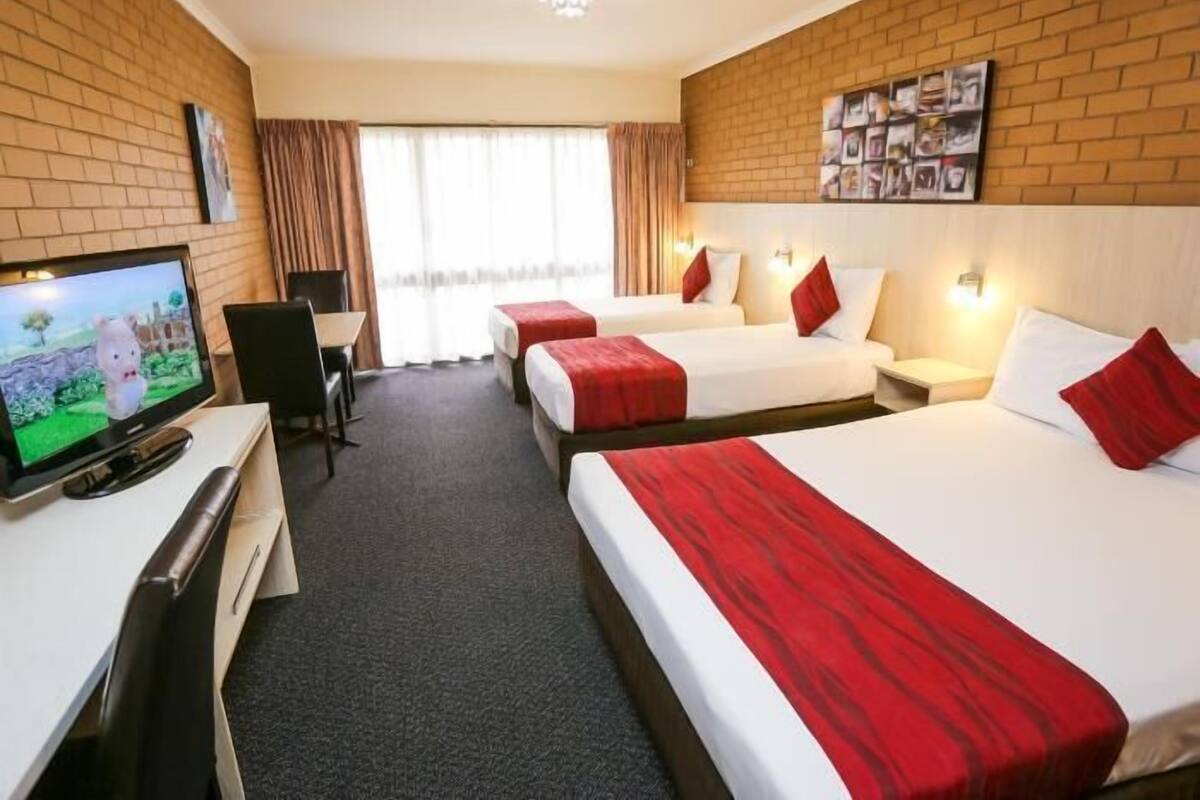A hotel room with two beds, a desk with a TV, and a brick wall.