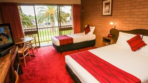 A hotel room with two beds, a TV, a desk, and a balcony with a view of palm trees. - River City Motel (Mildura)