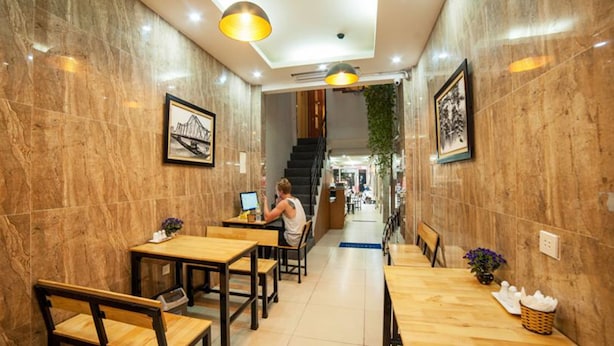 A restaurant with wooden tables and chairs, a person working on a laptop, and framed pictures on the walls. - Box Hotel (Hanoi)