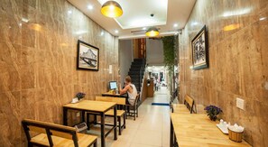 Ein Restaurant mit Holztischen und -stühlen, eine Person arbeitet an einem Laptop, und an den Wänden hängen gerahmte Bilder.