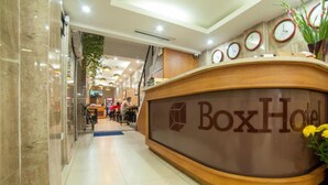 A reception desk with the name 'Box Hotel' and a logo, surrounded by clocks and a potted plant. - Box Hotel (Hanoi)
