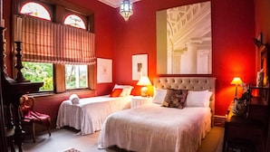 A hotel room with two beds, a large window with curtains, a chandelier, and a painting on the wall. - Archer House B&B (Westport)