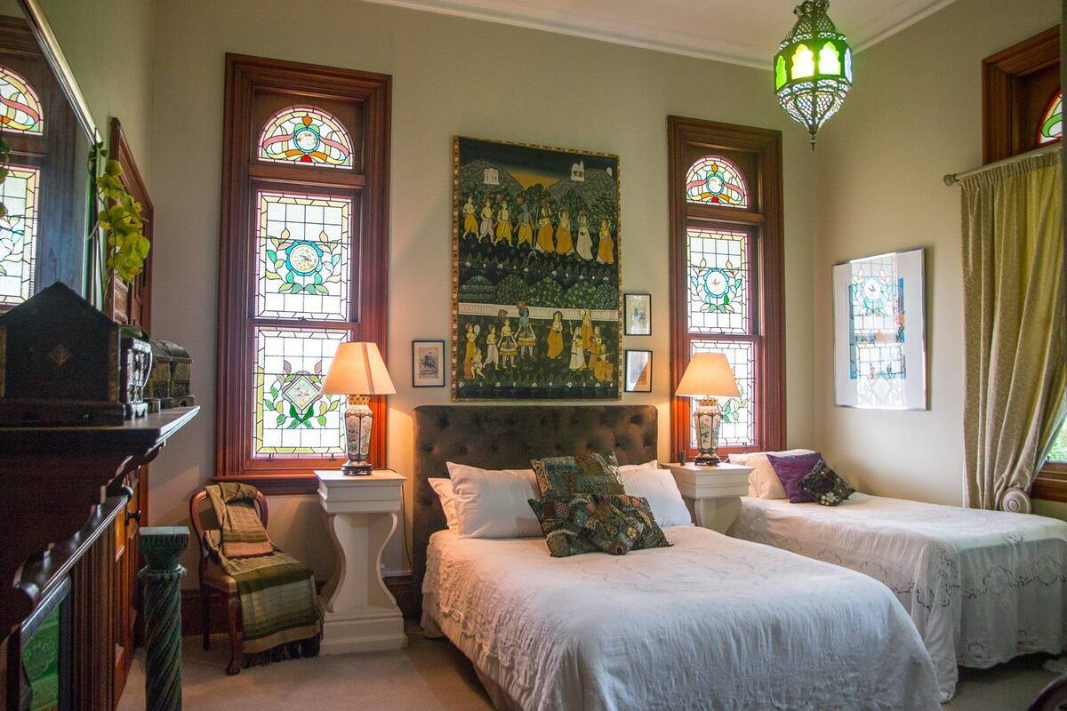 A room with two beds, a large painting, and stained glass windows.