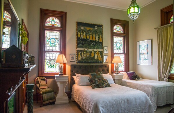 A room with two beds, a large painting, and stained glass windows.