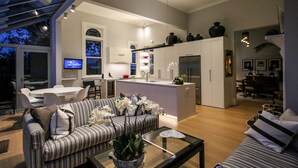 A modern living room with a striped sofa, a coffee table with a plant, and a dining area with a TV. - Archer House B&B (Westport)