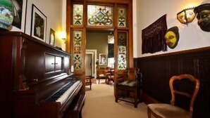 A room with a piano, wooden chairs, a stained glass window, and wall-mounted masks. - Archer House B&B (Westport)