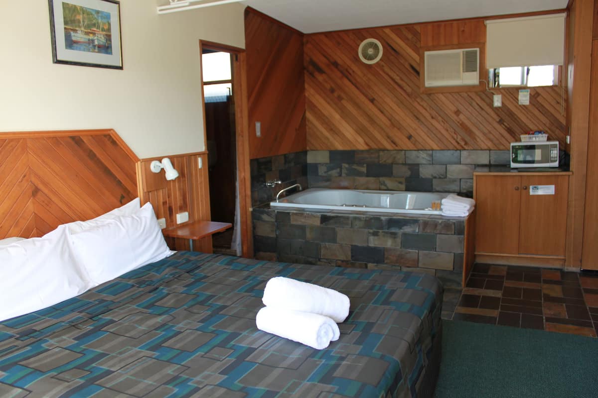 A hotel room with a bed, a bathroom with a bathtub, a microwave, and a small table.