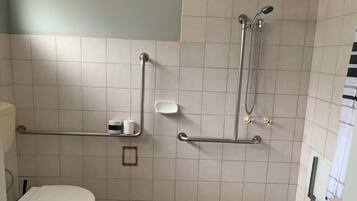 A bathroom with a toilet, grab bars, a shower, and a soap dish.