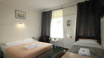 Une chambre d’hôtel avec deux lits, une petite table, une chaise, un bureau, un miroir et une fenêtre avec des rideaux.
