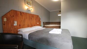 A bedroom with a wooden headboard, a bed with a grey blanket, a chair, and a bathtub.