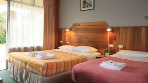 A hotel room with two beds, a wooden headboard, a window with curtains, and a small plant on the nightstand. - Pelicans Motel San Remo (San Remo)