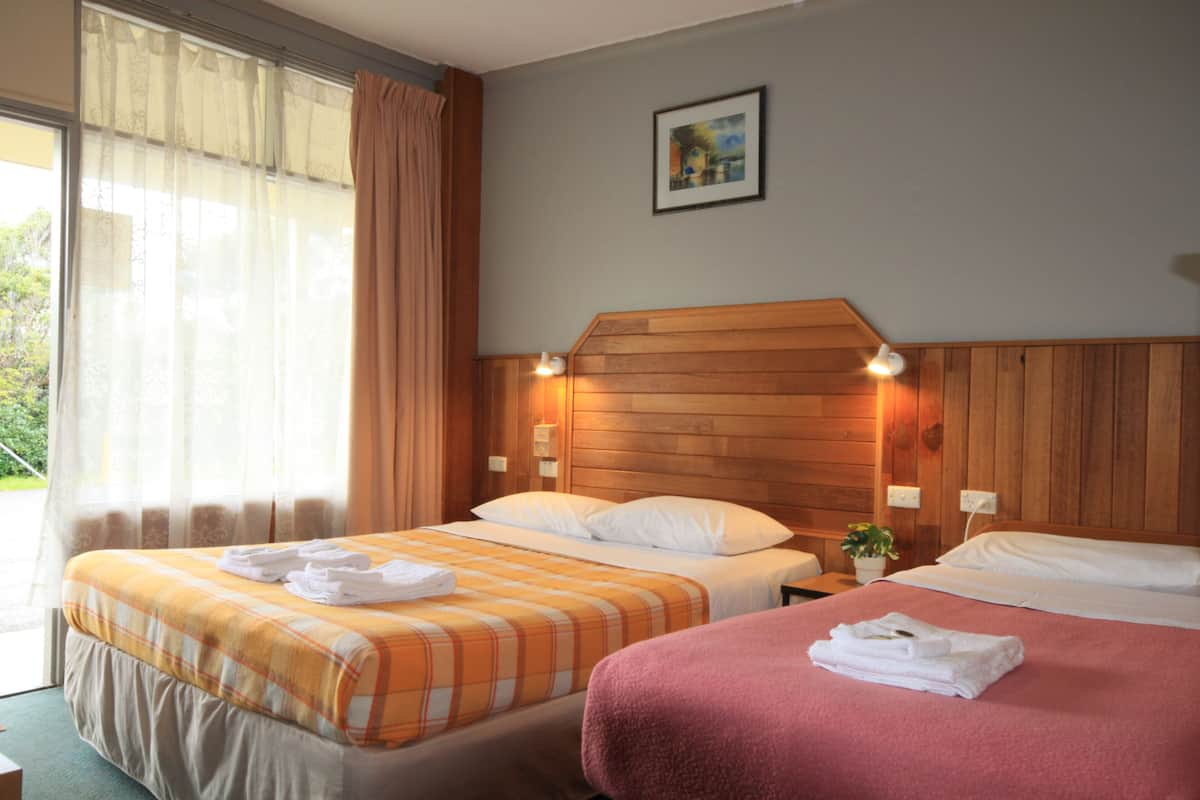 A hotel room with two beds, a wooden headboard, a window with curtains, and a small plant on the nightstand.