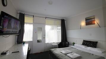 Et hotelværelse med seng, fjernsyn, skrivebord, stol og et vindue med gardiner.