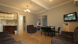 A living room with a TV, a dining table, and a couch. - Pelicans Motel San Remo (San Remo)