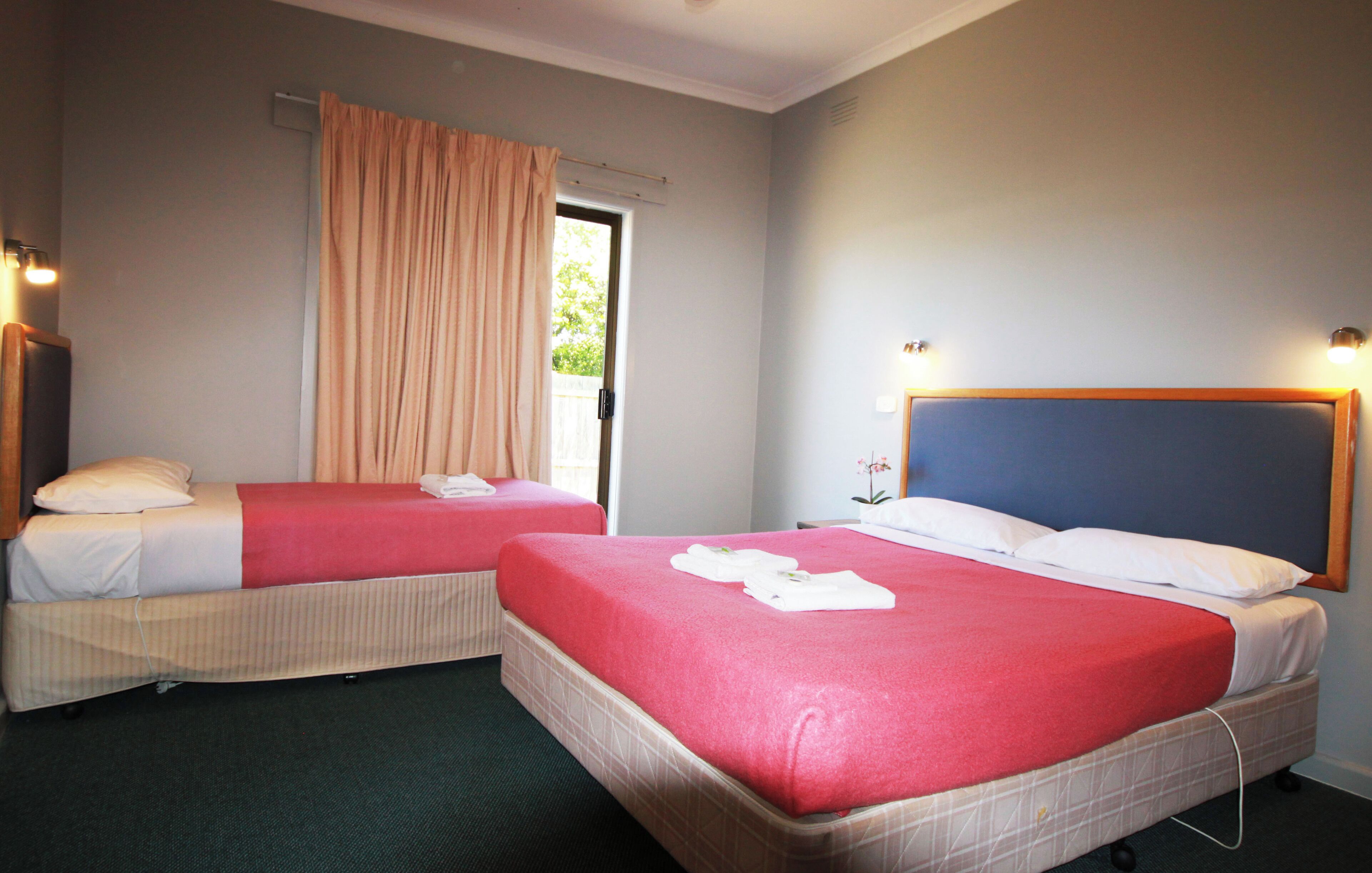 Two single beds with red bedding, a wooden headboard, and a window with curtains.