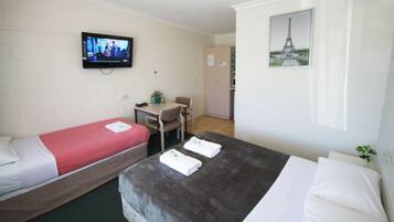 A hotel room with two beds, a desk, a chair, a television, and a picture of the Eiffel Tower.