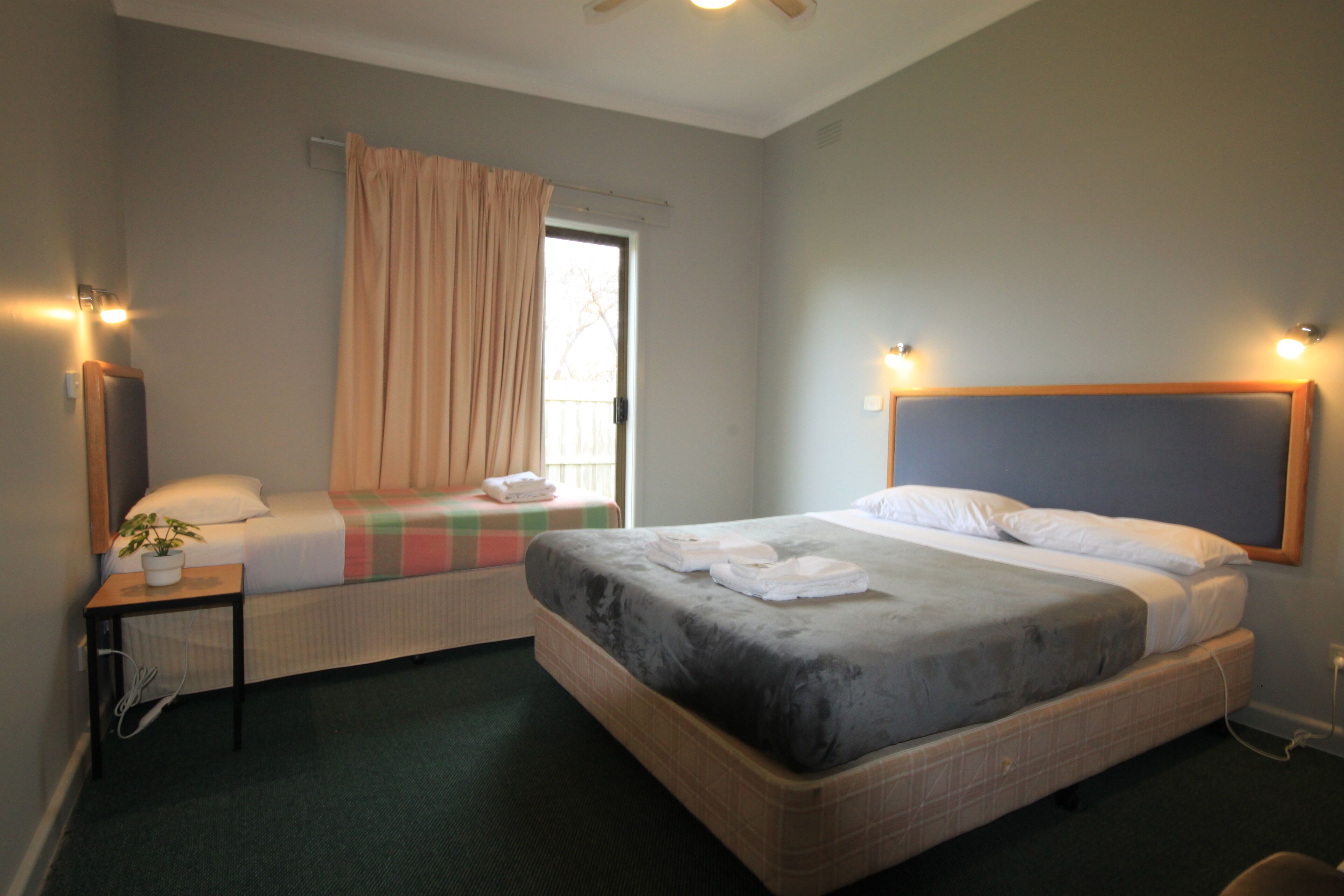 Une chambre d’hôtel avec deux lits, une fenêtre avec des rideaux, une table de chevet avec une plante et des lampes fixées au mur.